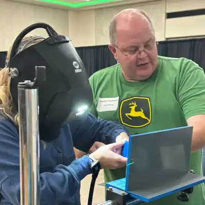 Image of a student welding with volunteer looking on