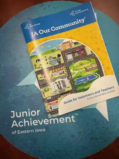The image showcases a Junior Achievement Our Community Program kit, neatly arranged on a table. The kit includes various educational materials: colorful lesson plans, engaging activity worksheets, and a set of interactive cards featuring community roles and civic responsibilities. There is also a small globe and a chart illustrating the voting process. All items are brightly colored and designed to capture students' attention, emphasizing hands-on learning about civic engagement and the electoral process. The background is neutral to keep the focus on the kit contents.